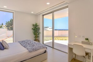 A modern bedroom with a bed, a desk, and a large sliding glass door leading to a balcony.