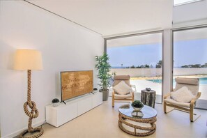A modern living room with a TV, a lamp, and a view of a pool and beach.