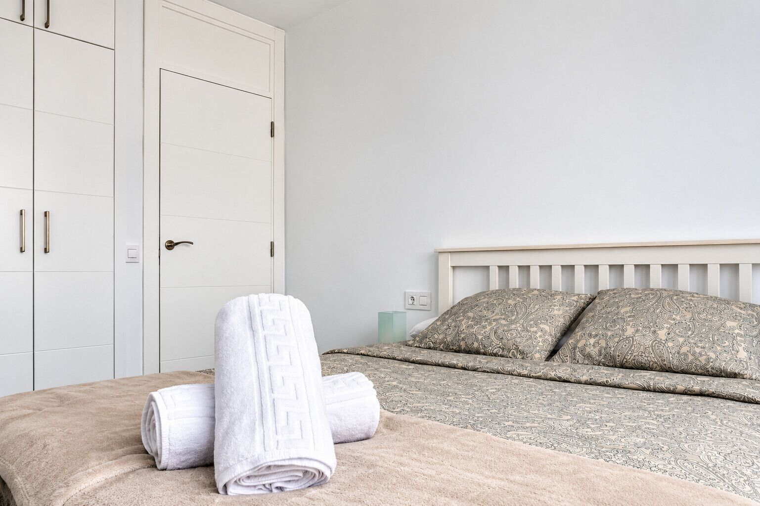 A bedroom with a bed, pillows, a rolled towel, and a wardrobe.