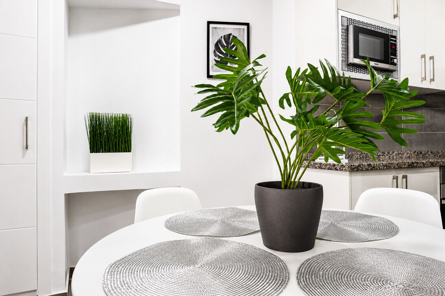 A modern kitchen with white cabinetry, a black microwave, and a potted plant.