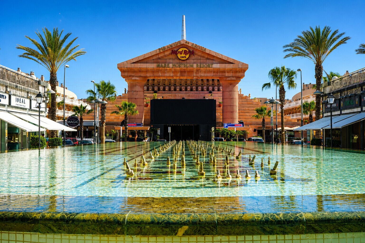 A hotel with a large pool, palm trees, and a Hard Rock Cafe.