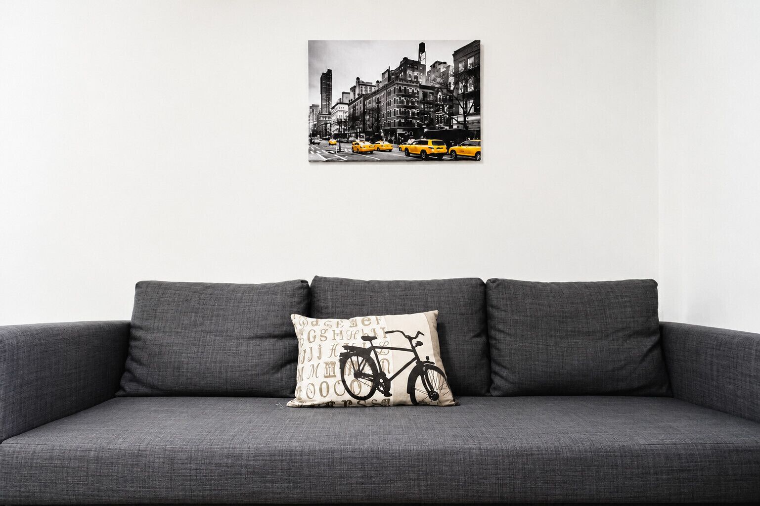 A grey sofa with a single patterned pillow and a black and white cityscape artwork above it.