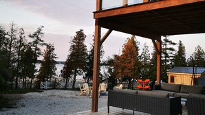 Een houten terras met buitenmeubilair, een overdekte barbecue en uitzicht op bomen en een gebouw op de achtergrond.
