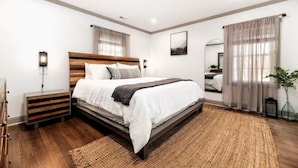 A modern bedroom with a wooden bed, bedside tables, a large mirror, and a view of the outdoors. - Cozy Escape! Modern/Luxe style w/2 Master en Suites-Fireplace-Fenced- SouthPark! (Charlotte)