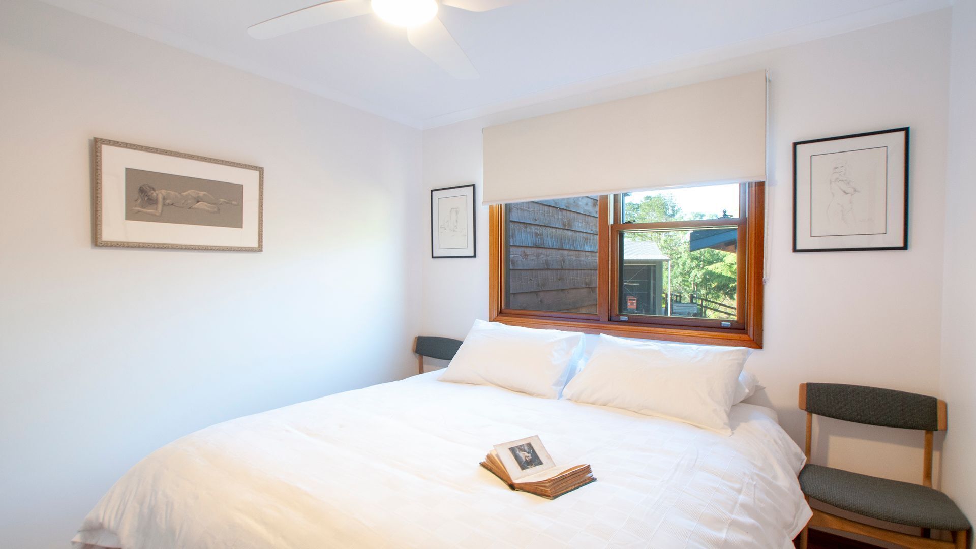 Une chambre avec un grand lit, une fenêtre donnant sur un paysage verdoyant et deux tableaux encadrés accrochés au mur.