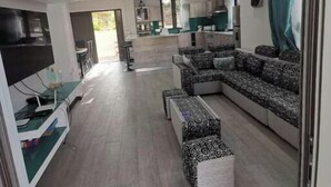 A modern living room with a sectional sofa, a flat-screen TV, and a dining area with a kitchen in the background. - Splendid 4-bedrooms villa private pool near beach (Flic en Flac)