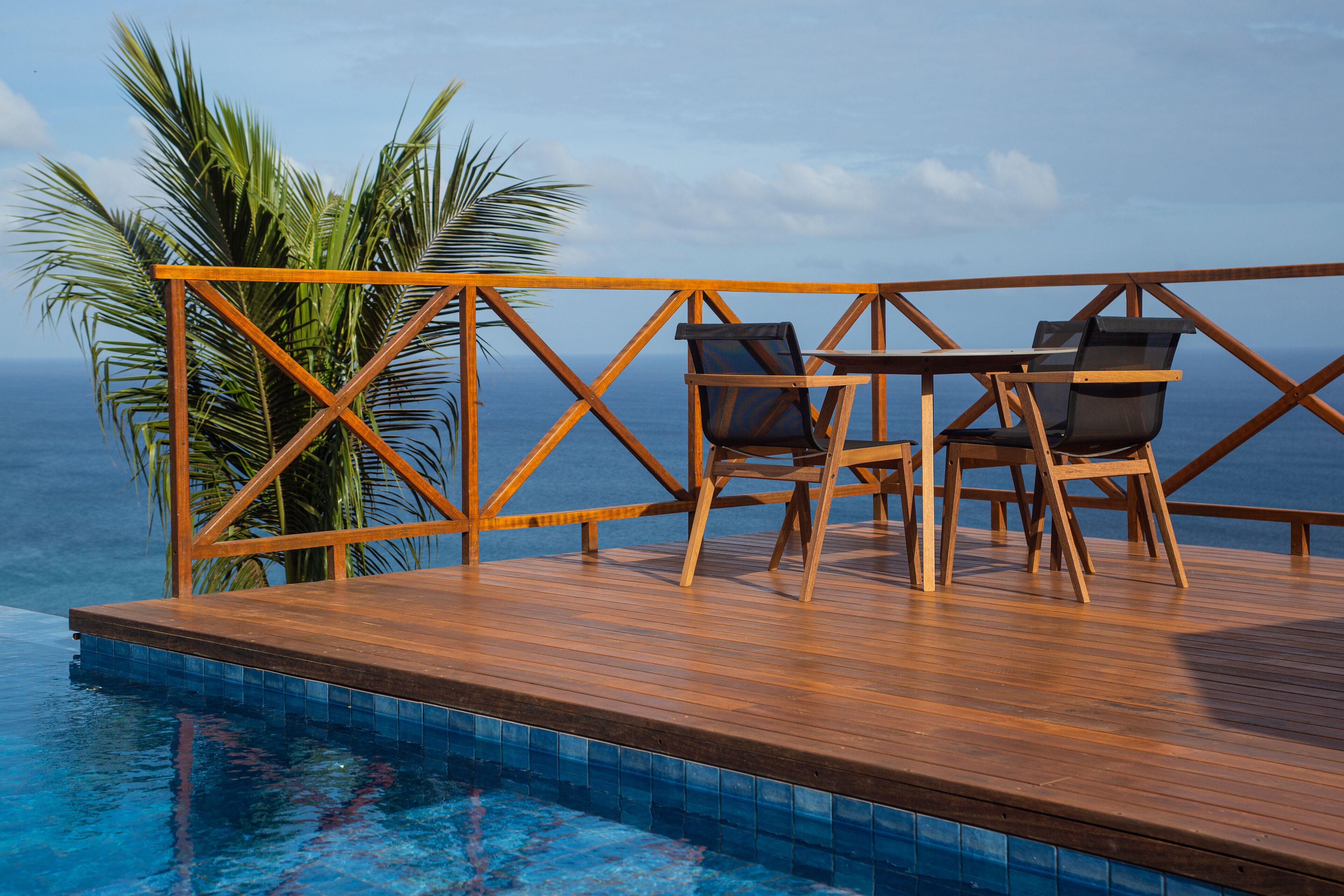 Terraza de madera con piscina, dos sillas y una palmera.