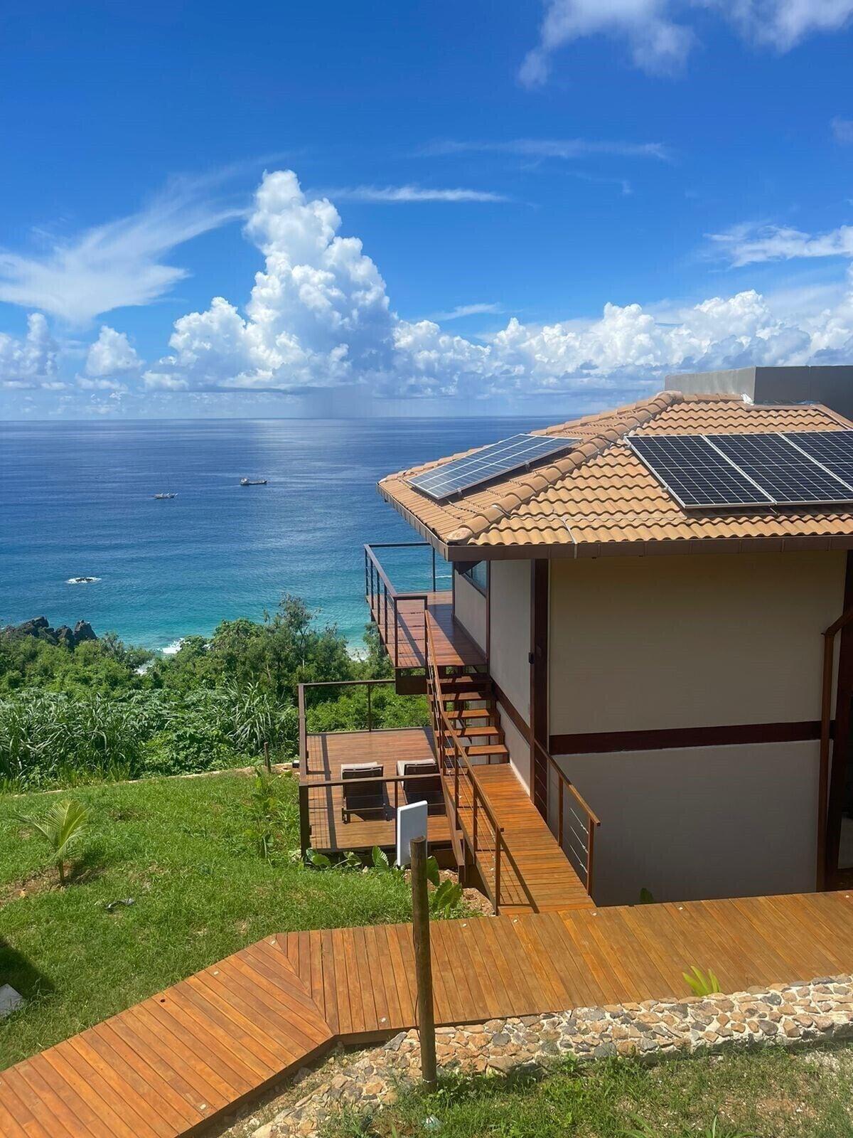 A modern house with a wooden deck, solar panels, and a view of the ocean.
