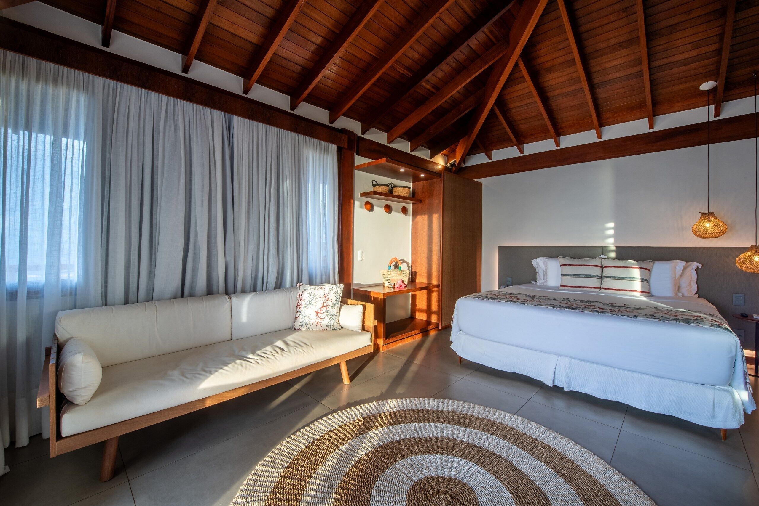 A room with a wooden ceiling, a sofa, a bed, a small table, and a hanging light fixture.