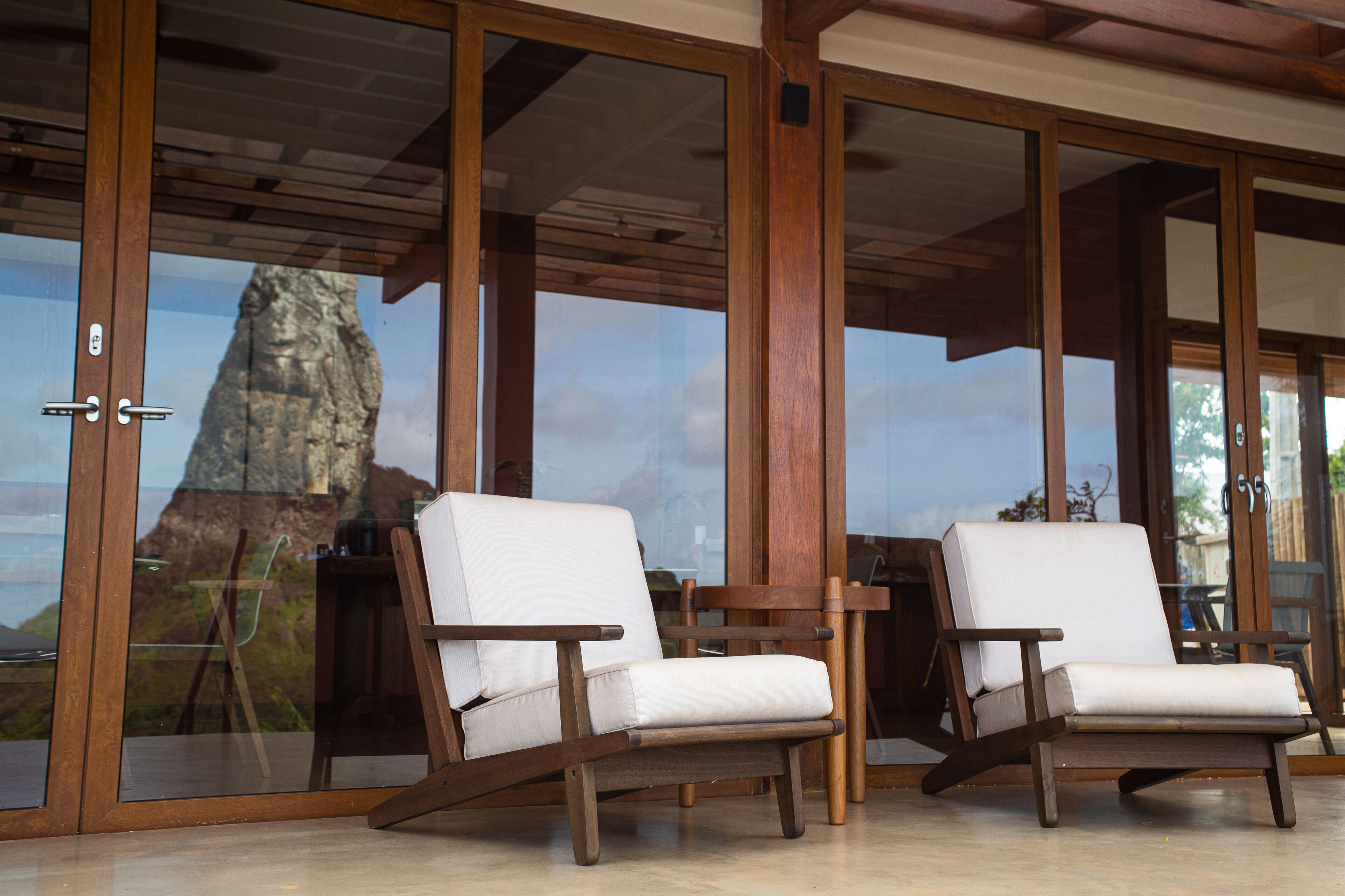 Two wooden lounge chairs with white cushions in a room with large glass doors.