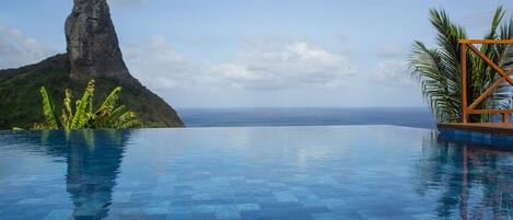 A infinity pool with a clear view of the ocean and a mountain in the background.