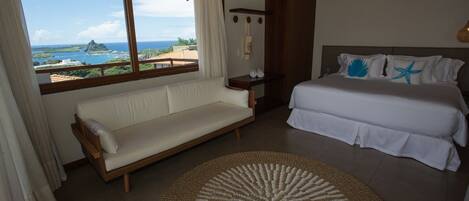 A bedroom with a bed, a sofa, a round woven rug, and a view of the ocean.