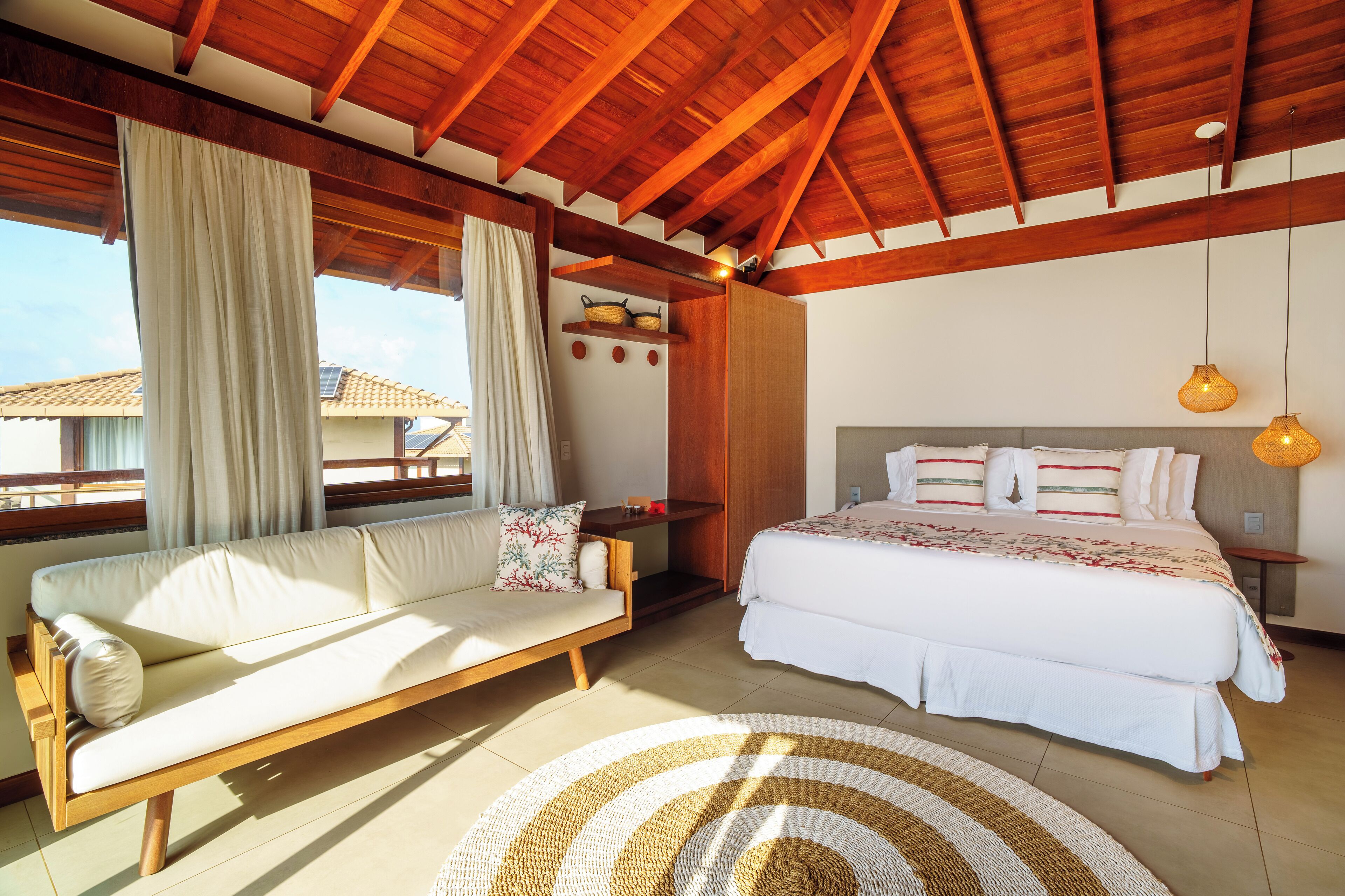 A bedroom with a wooden ceiling, a bed with white bedding, a sofa with cushions, and a round woven rug.