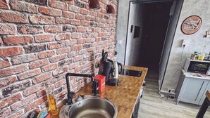 A kitchen with a brick wall, wooden countertop, stainless steel sink, and red bar stool.
