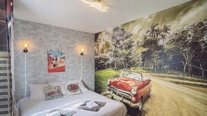 A bedroom with a bed, a wall mural of a red car on a road, and two wall-mounted lamps.