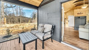 Um deck de madeira com sofá e mesa, uma janela grande e vista para um jardim.