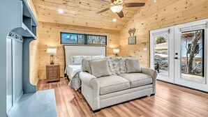 Ein gemütliches Schlafzimmer mit Bett, Sofa, Deckenventilator und Fenster mit Blick ins Freie.
