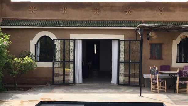 A pool area with a clear view of the pool, a covered patio with chairs, and a door leading to an interior space. - Villa Piscine Marrakech (Marrakech)