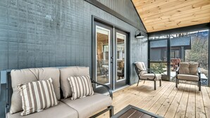 Een overdekt buitengebied met een houten terras, een bank met gestreepte kussens en twee stoelen.