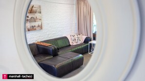 Ein Wohnzimmer mit einer Eckcouch, einem kleinen Beistelltisch und einer weißen Ziegelwand mit einem gerahmten Bild.