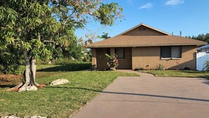 A single-story house with a brown roof, a front yard with a tree, and a driveway leading to the entrance. - Heated Pool, Shopping, Restaurants, Beach's, Southern Exposure (Naples)