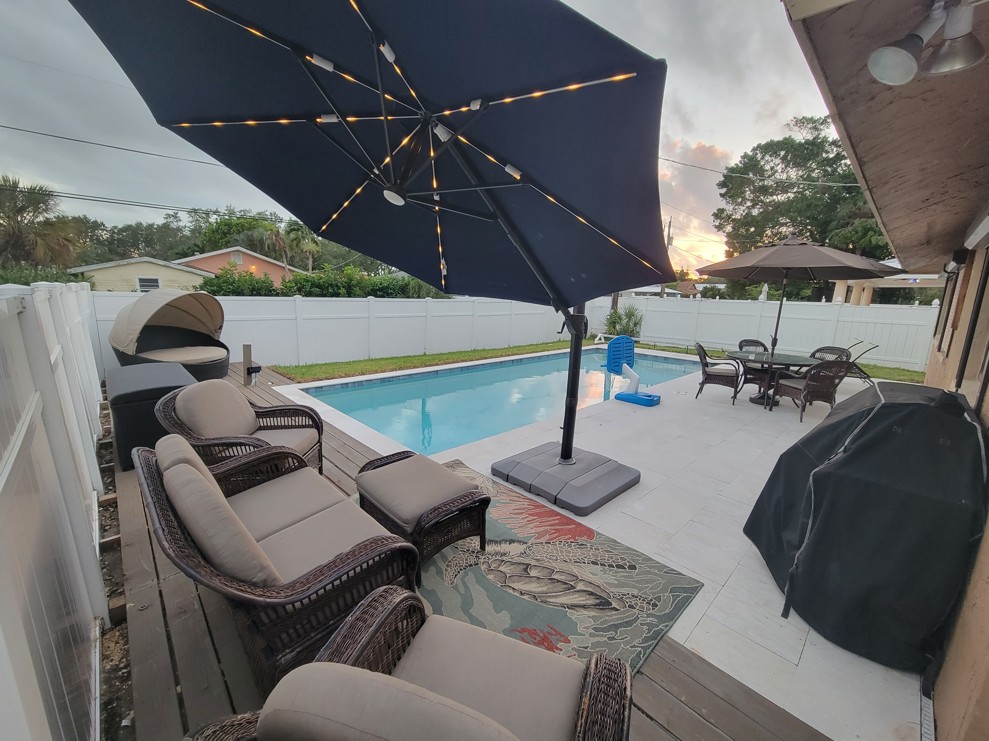 A backyard with a swimming pool, outdoor furniture, and a barbecue grill.