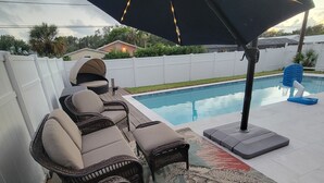 A poolside area with wicker lounge chairs, a patterned rug, and an umbrella. - Heated Pool, Shopping, Restaurants, Beach's, Southern Exposure (Naples)