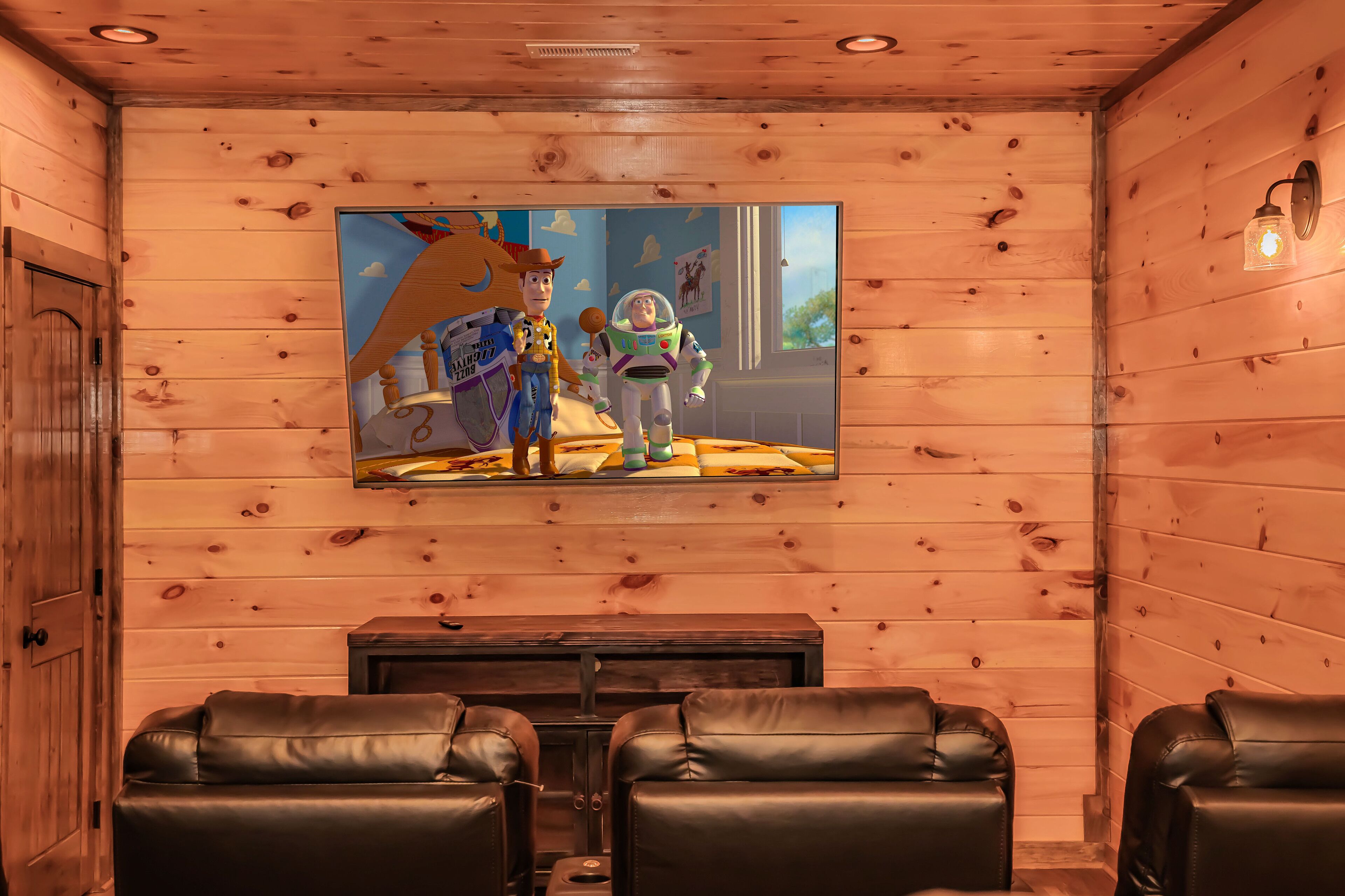Una stanza con rivestimenti in legno, un grande schermo televisivo che mostra personaggi animati, sedute in pelle e un tavolino.