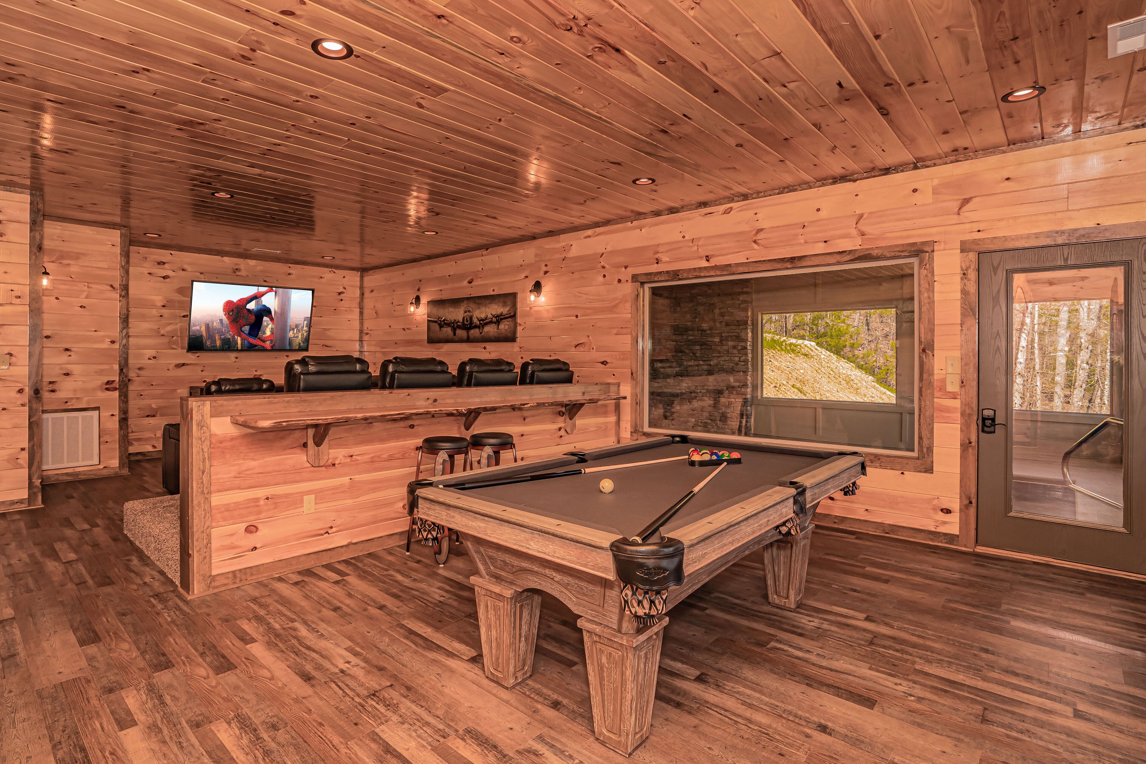 A wooden interior with a pool table, bar area, and a television displaying a movie scene.