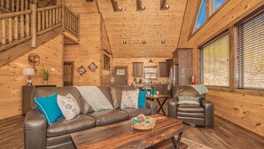 A wooden cabin interior with a leather sofa, a coffee table, and a dining area. - To Infinity And Beyond: Indoor-Pool, VIEWS, Theater, Game Room, Hot Tub, WiFi, close to Attractions! (Sevierville)