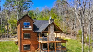A two-story wooden cabin with a stone chimney, a balcony, and a deck with outdoor seating. - To Infinity And Beyond: Indoor-Pool, VIEWS, Theater, Game Room, Hot Tub, WiFi, close to Attractions! (Sevierville)