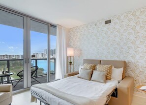A hotel room with a large bed, a balcony with a view, and a patterned wall.