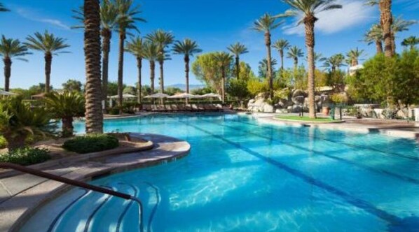 Relax by the resort pool surrounded by lush greenery and palm trees, with lounge chairs and umbrellas providing shade.