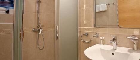 Een badkamer met een douche met glazen wand, een wit wastafeltje en een spiegel erboven.