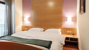 A hotel room with a wooden headboard, a bed with white linens, two bedside lamps, and a small nightstand with a plant.