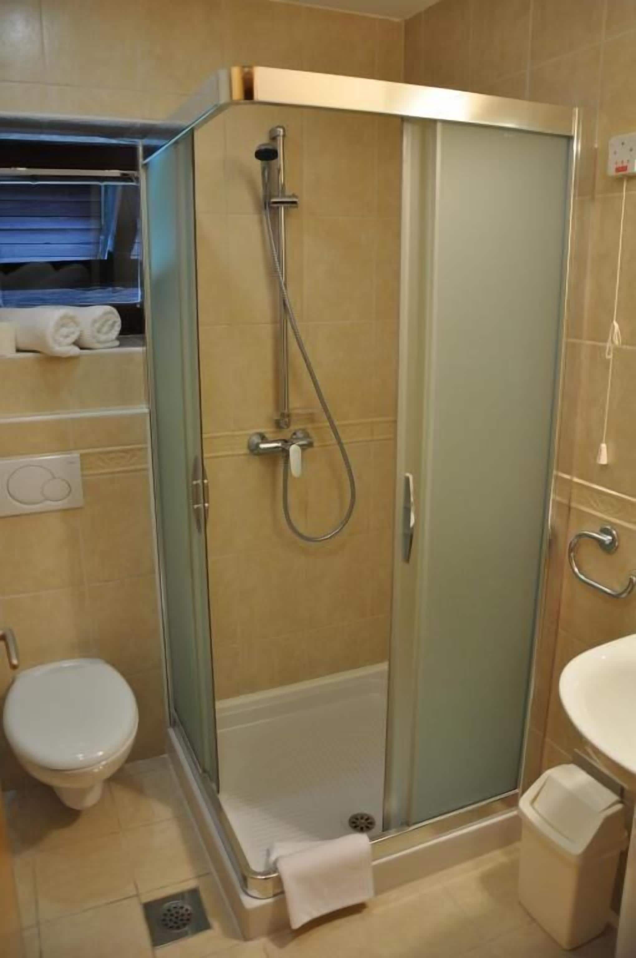 Een douchecabine met glazen wanden, een handdoek op de vloer, een toilet en een wastafel.