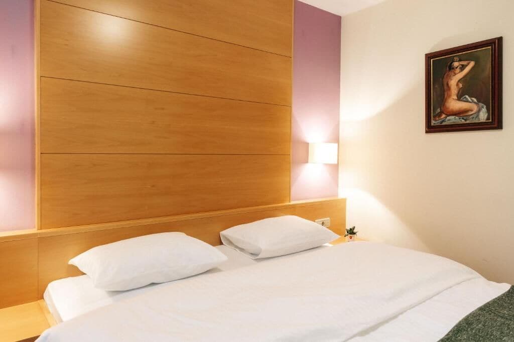 Une chambre d’hôtel avec une tête de lit en bois, du linge de lit blanc, une lampe fixée au mur et un tableau encadré.