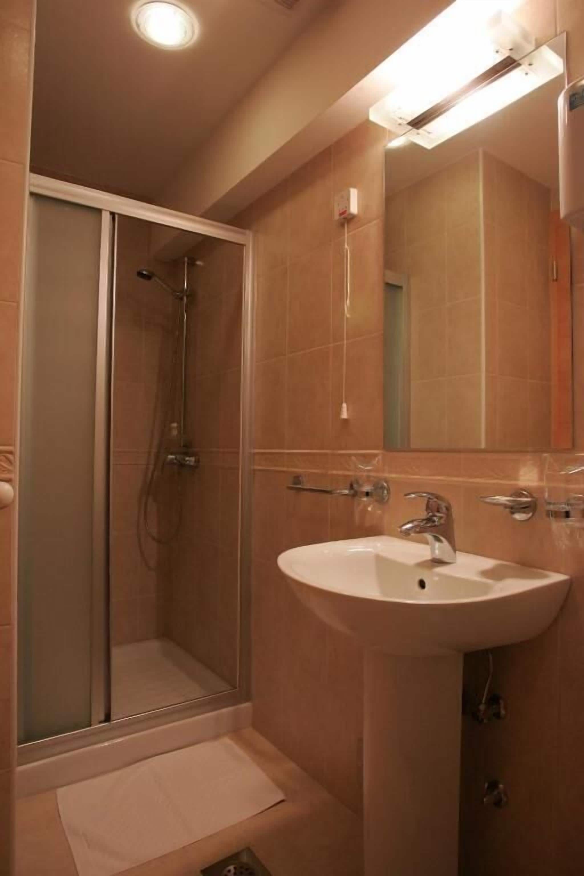 A bathroom with a glass-enclosed shower, a sink with a mirror, and beige tiles.