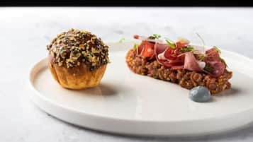 Een bord met een muffin bezaaid met zaden en een schaal met vlees en groenten.