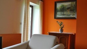 A room with two white armchairs, a small table with a plant, and a framed painting on the orange wall.