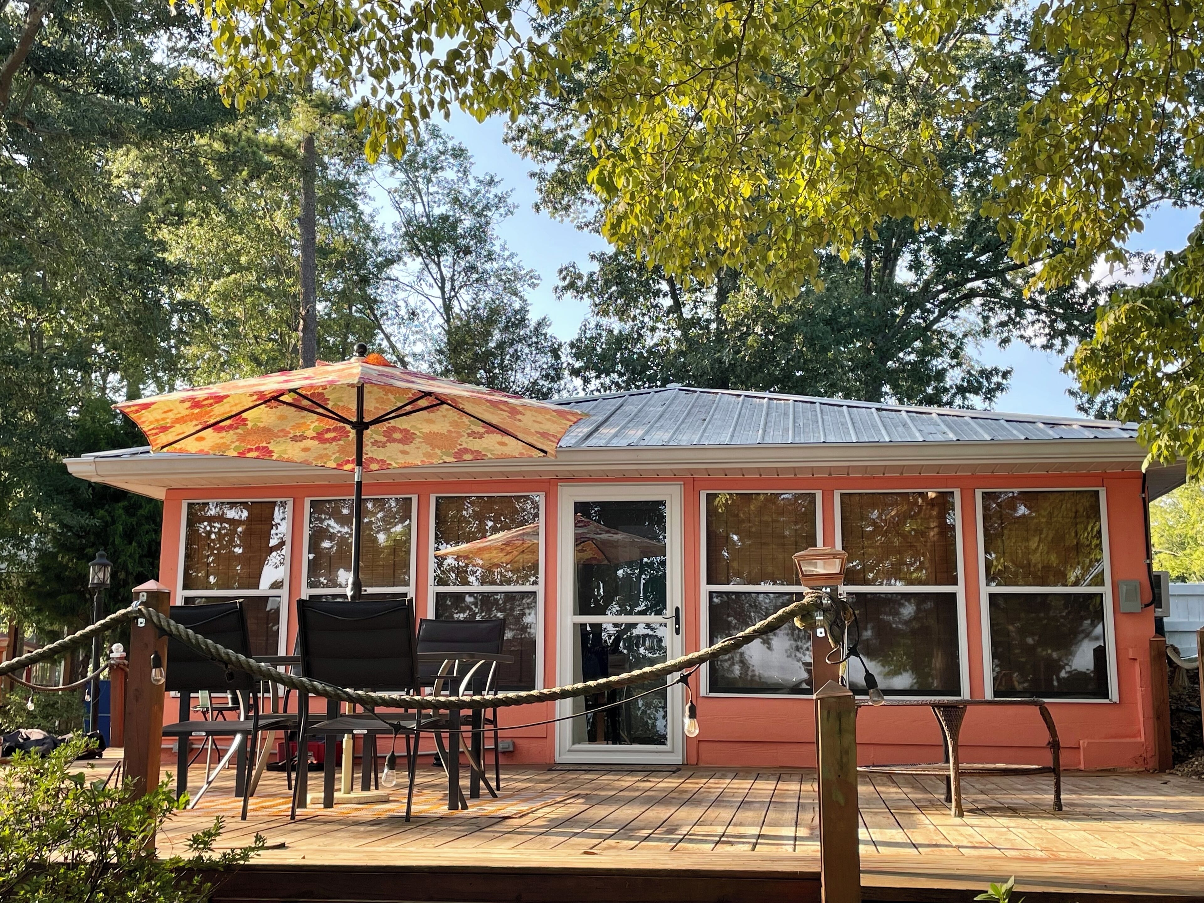 A small building with large windows, a deck with chairs, and an umbrella.