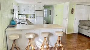Una cocina con armarios blancos, una isla central con taburetes, un microondas y un refrigerador.
