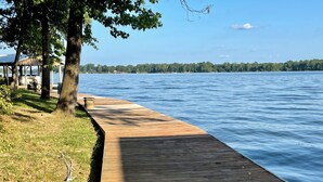 Un muelle de madera se adentra en un lago tranquilo, con una zona cubierta de hierba y árboles en un lado.
