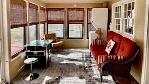 Habitación compacta con sofá rojo, una mesita con una silla y una pequeña zona de kitchenette.