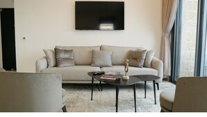 Una sala de estar con un sofá color beige, una mesa de centro y un televisor de pantalla plana montado en la pared.