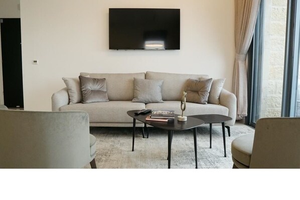 Een woonkamer met een beige bank, een salontafel en een flatscreen televisie aan de muur.
