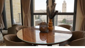 Una mesa redonda de vidrio con un centro de mesa tejido, rodeada de sillas tapizadas, en una habitación con ventanas amplias y vistas a un edificio.