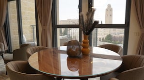 Een ronde glazen tafel met een geweven decoratie, omringd door beklede stoelen, in een kamer met grote ramen en uitzicht op een gebouw.