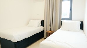 Een hotelkamer met twee éénpersoonsbedden, een klein rond tafeltje en een raam met gordijnen.