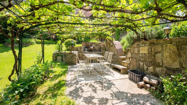 Eine Terrasse mit Tisch und Stühlen, eine Steinmauer und eine Feuerstelle.
